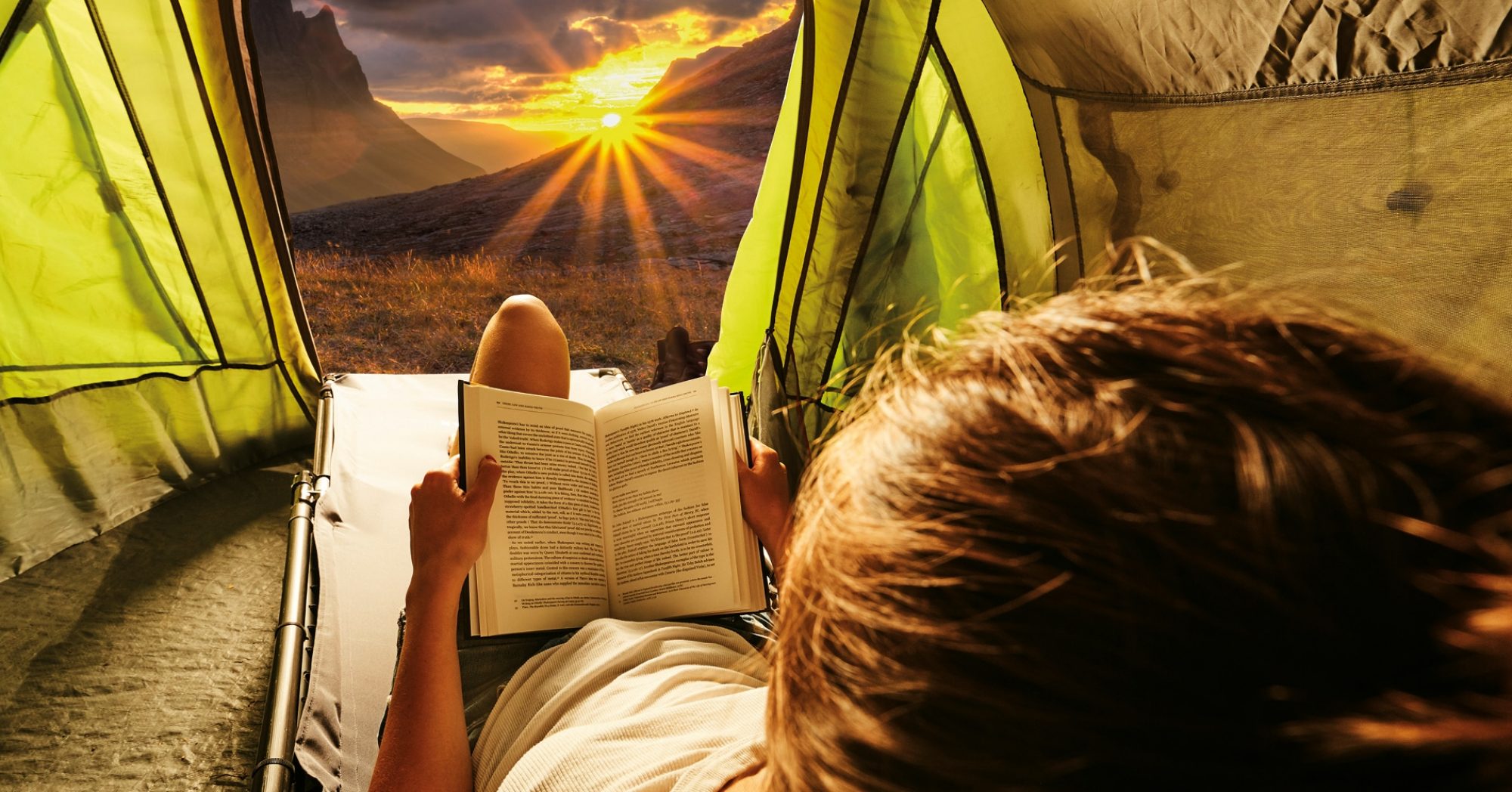 Girl relaxing and reading on LayBakPak recliner camp bed inside a tent