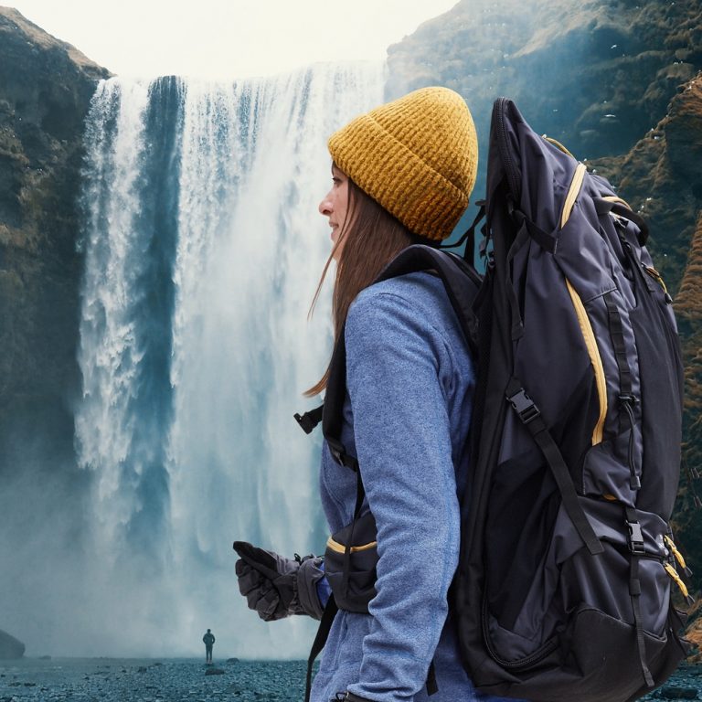 woman wearing LayBakPak backpack standing beside a waterfall