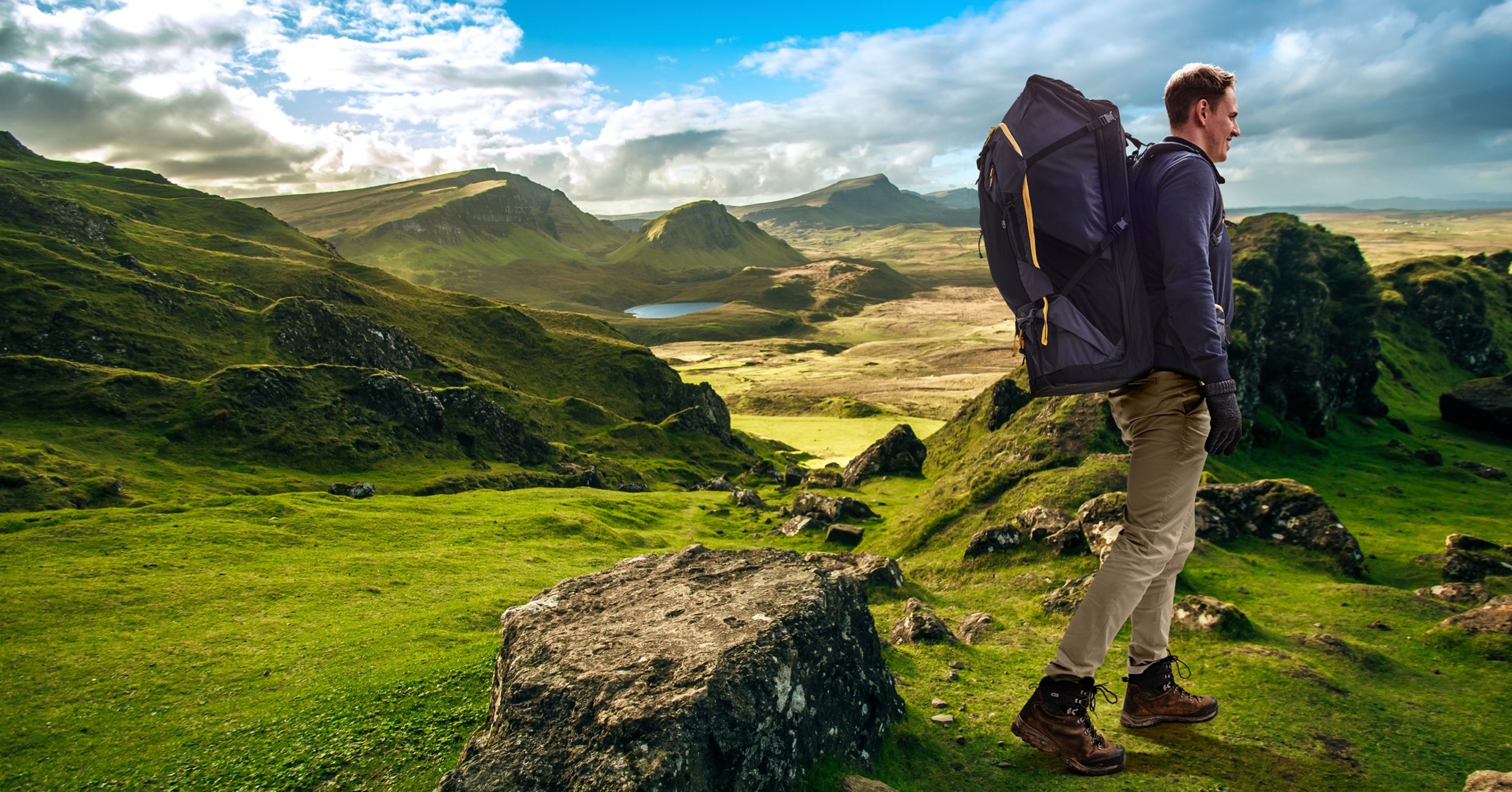 Man wearing fully loaded LayBakPak backpack hiking across rocky hill top