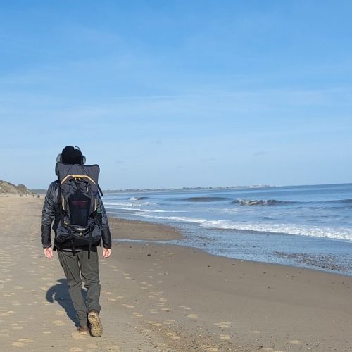 Man walking along empty sandy beach wearing LayBakPak