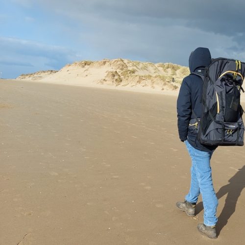 Man wearing LayBakPak backpack walking along beach beside sand dunes