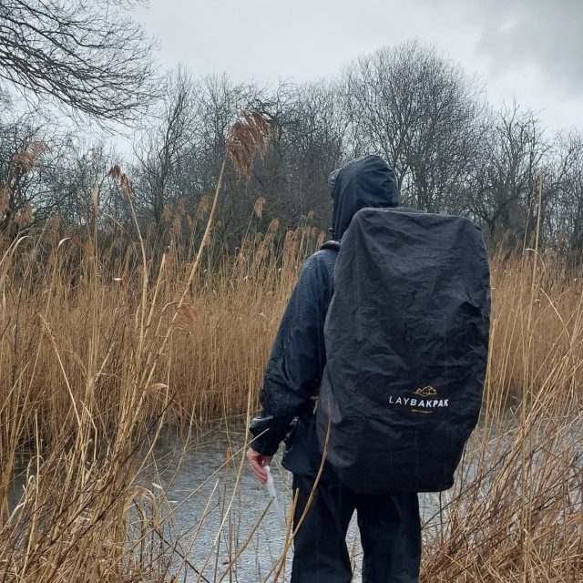 Man wearing LayBakPak with rain cover looking across river to reed beds