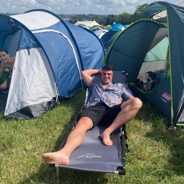 Man relaxing on LayBakPak lounger surrounded by tents at Glastonbury
